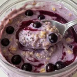 Glass jar filled with creamy blueberry overnight oats, topped with fresh blueberries, chia seeds, and a drizzle of maple syrup.