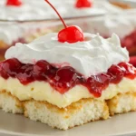 A generous slice of homemade Heaven on Earth No Bake Cake on a white plate, showing visible cubes of angel food cake held together with creamy pudding and topped with cherry filling and whipped cream.