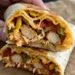 A homemade Chipotle Ranch Grilled Chicken Burrito sliced in half on a rustic wooden board, showing the juicy grilled chicken, melted cheese, and creamy sauces inside.