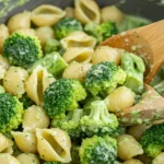 A close-up shot of healthy broccoli pasta in a gray skillet, featuring shell pasta coated in a creamy green broccoli sauce and topped with grated Parmesan cheese.